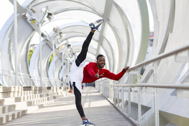 Smiling sportsman exercising while doing the splits on walkway - JCCMF00185