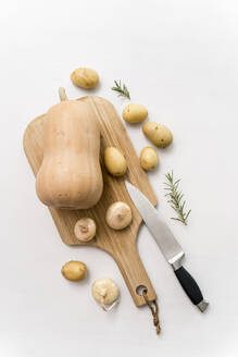 Studioaufnahme von Kürbis, rohen Kartoffeln und Zwiebeln auf einem Schneidebrett - MAUF03649
