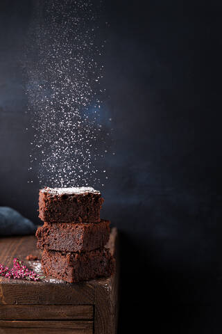 Yummy homemade chocolate brownies pieces stacked on table and sprinkled with white sugar powder against dark background stock photo