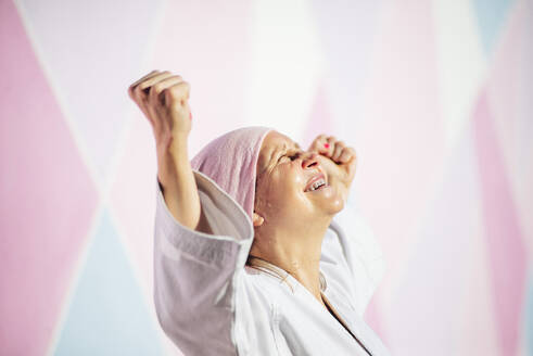Entschlossen reife Frau in rosa Kopfbedeckung und Gürtel kämpfen Karate in Krebs Kampf Konzept tun Sieg Geste auf der Straße auf rosa Wand nach oben schauen - ADSF19060