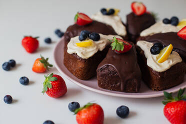 Nahaufnahme köstlicher hausgemachter Schokoladenkuchen mit weißer und Schokoladencreme, dekoriert mit frischen Beeren und Zitronenscheiben und in Stücke geschnitten - ADSF19151