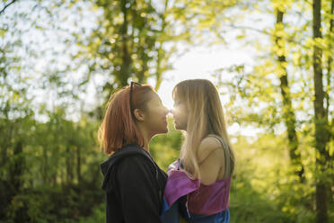 Junges lesbisches Paar, das im Wald stehend eine Romanze hat - MTBF00791