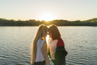 Lesbisches Paar steht von Angesicht zu Angesicht am See bei Sonnenuntergang - MTBF00798