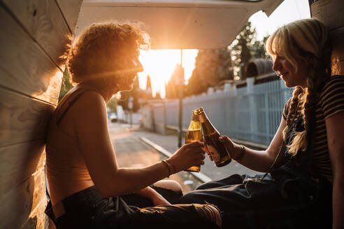 Junges weibliches Paar stößt mit Bierflaschen auf dem Rücksitz eines Lieferwagens an - CUF56607