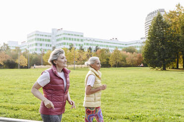 Lächelnde Freundinnen laufen im öffentlichen Park an einem sonnigen Tag - VYF00354