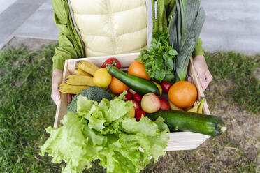 Ältere Frau mit Holzkiste gefüllt mit gesunden Lebensmitteln über Gras - VYF00373