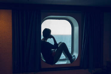 Frau betrachtet die Aussicht, während sie am Schiffsfenster sitzt - MAMF01476