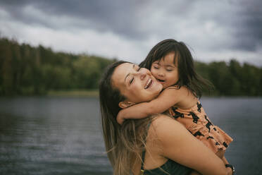 Smiling down syndrome daughter embracing mother against lake - MASF20978