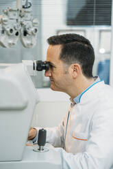 Male optometrist looking phoropter in clinic - MPPF01298