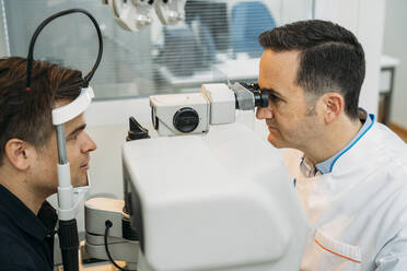 Mature optometrist examining patinet's eye through phropter in clinic - MPPF01299