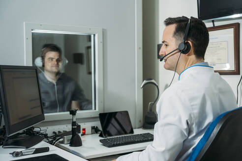 Male audiologist taking ear exam of patient wearing headphones in clinic - MPPF01300