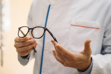 Male optometrist holding eyeglasses in clinic - MPPF01305