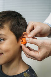 Männlicher Audiologe, der einem Kind in der Klinik Hörluft ins Ohr einbläst - MPPF01307