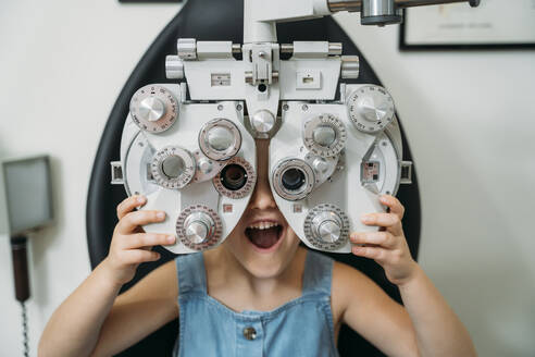 Cheerful girl with mouth open holding eye test equipment in clinic - MPPF01309