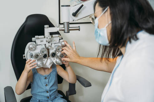 Optikerin untersucht die Augen von Mädchen durch einen Propther in der Klinik während COVID-19 - MPPF01310