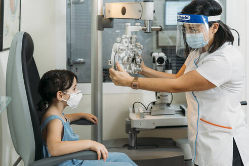 Mid adult female optometrist adjusting propther for medical test at clinic during COVID-19 - MPPF01311