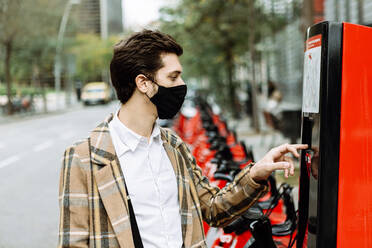 Young man in face mask renting bicycle in city - XLGF00885