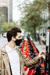 Young man in face mask renting bicycle in city - XLGF00886