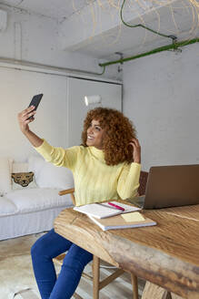 Smiling businesswoman with hand in hair taking selfie at home - VEGF03309