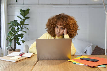 Bored businesswoman with hand in hair working on laptop at home - VEGF03310