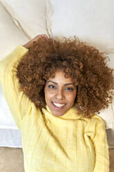 Lächelnde Frau mit braunen Haaren lehnt auf dem Sofa im Wohnzimmer - VEGF03315