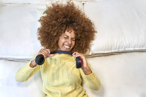 Woman with eyes closed playing with headphones after work in bedroom - VEGF03317