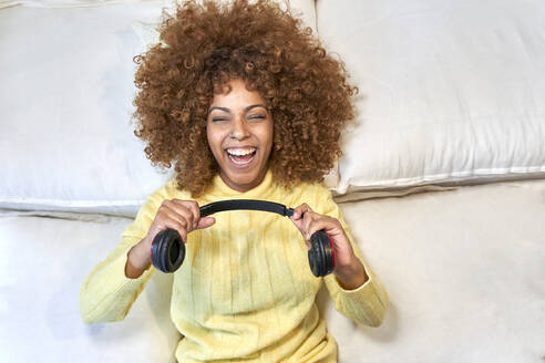 Laughing woman playing with headphones after work in bedroom - VEGF03318