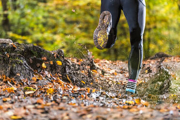 Männlicher Trailrunner, der durch den Schlamm im Herbstwald am Kappelberg läuft, Deutschland - STSF02727