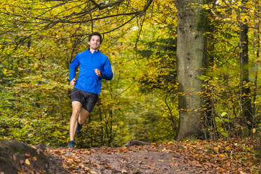 Lächelnder männlicher Sportler beim Trailrunning über Schlamm im Herbstwald am Kappelberg, Deutschland - STSF02729