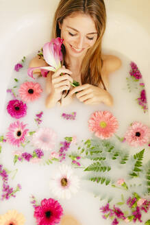 Smiling woman lying in bathtub while taking milkbath at spa - GMLF00901