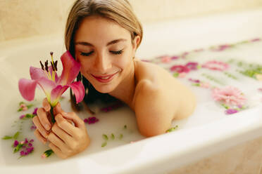 Glückliche Frau mit Blumen in der Badewanne liegend im Spa - GMLF00910