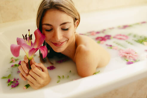 Happy woman with flowers lying in bathtub at spa - GMLF00910