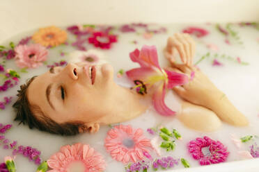 Junge Frau inmitten von Blumen, die ein Milchbad in einer Badewanne im Spa nimmt - GMLF00915