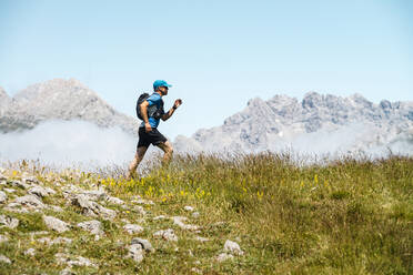 Älterer Sportler beim Trailrunning in den Bergen auf einer Wiese vor blauem Himmel - JMPF00707