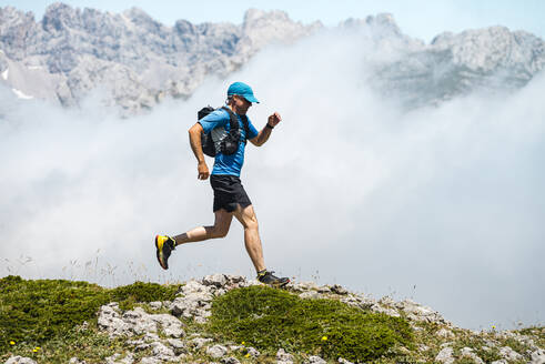 Mature sportsman trail running through foggy mountains - JMPF00709