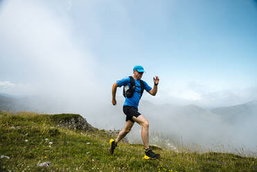 Älterer Sportler beim Trailrunning in den Bergen auf einer Wiese - JMPF00710