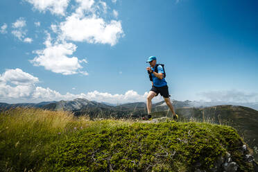 Älterer Sportler beim Trailrunning in den Bergen auf einer Wiese vor blauem Himmel - JMPF00711