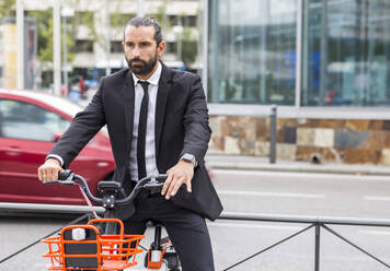 Porträt eines bärtigen Geschäftsmannes auf einem Fahrrad sitzend - JCCMF00199