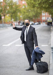 Geschäftsmann mit Gesichtsschutzmaske winkt ankommendem Auto zu - JCCMF00221