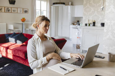 Schwangere Geschäftsfrau arbeitet am Laptop am Schreibtisch zu Hause - MRAF00601