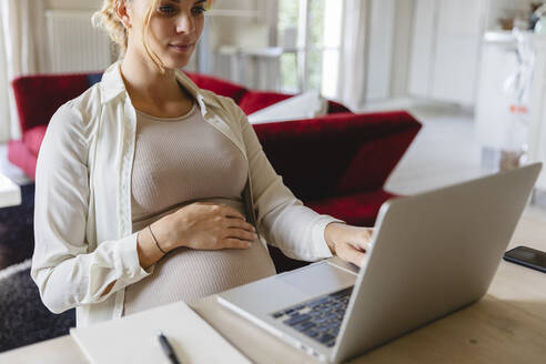 Schwangere Freiberuflerin mit Laptop im Wohnzimmer - MRAF00602