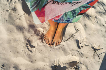 Mid adult woman with black nail polish on feet at beach on sunny day - JMPF00718