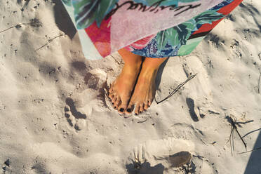 Mittlere erwachsene Frau mit schwarzem Nagellack an den Füßen am Strand an einem sonnigen Tag - JMPF00718