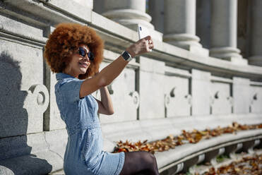 Lächelnde Frau macht ein Selfie am Alfonso Xii-Denkmal an einem sonnigen Tag, Parque Del Buen Retiro, Spanien - OCMF01875