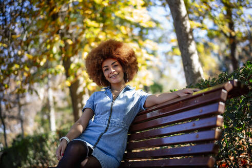 Glückliche Frau sitzt auf einer Bank in einem öffentlichen Park - OCMF01876