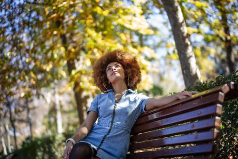 Mittlere erwachsene Frau, die beim Träumen auf einer Bank in einem öffentlichen Park nach oben schaut - OCMF01877