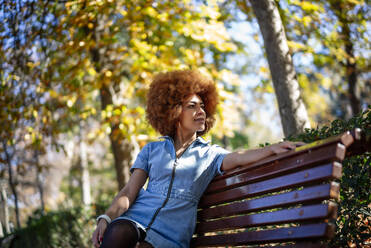 Thoughtful woman looking away while sitting on bench at public park - OCMF01878