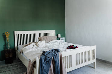 Unordentliches Bett mit Bettdecke und Kleidung im Schlafzimmer zu Hause - AFVF07842