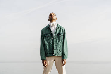 Young African man standing against sky and sea - AFVF07845