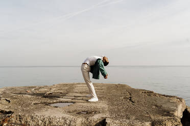 Young man bending back while standing on pier by sea - AFVF07847